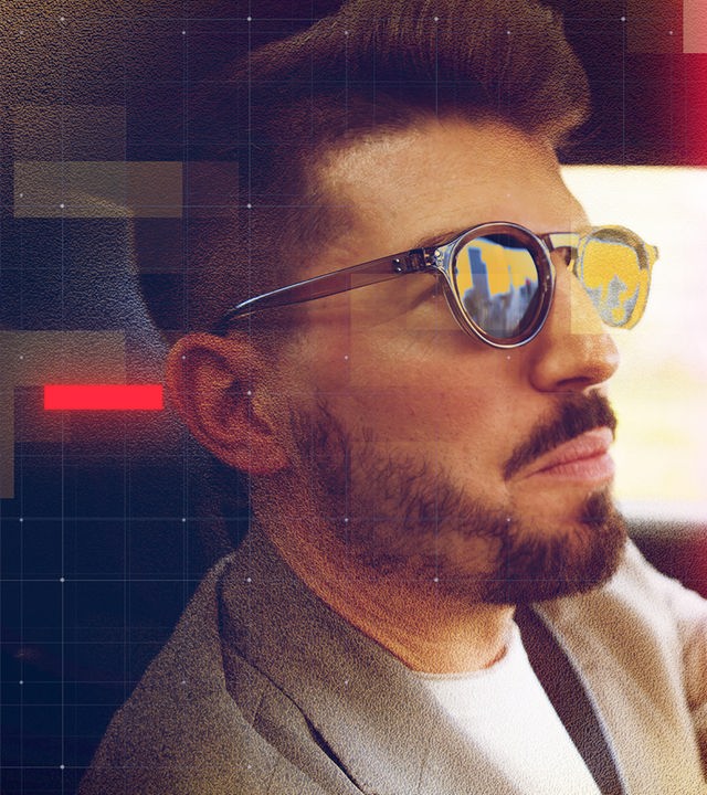 Eine männliche Person mit kurz geschnittenem Haar, Bart und Sonnenbrille sitzt am Steuer eines Sportwagens und blickt konzentriert nach vorn. Die Szene vermittelt den Eindruck eines professionellen Finanzhändlers, der Märkte beobachtet und Anlageentscheidungen trifft. In den verspiegelten Gläsern spiegeln sich goldfarbene Töne und eine angedeutete Stadtsilhouette, die das Thema Gold, Börse und Wertanlage aufgreifen. Über dem digital bearbeiteten Bild liegen halbtransparente rote und goldene Grafikelemente sowie ein feines grafisches Raster-Overlay, wodurch ein modernes, redaktionelles Erscheinungsbild entsteht.