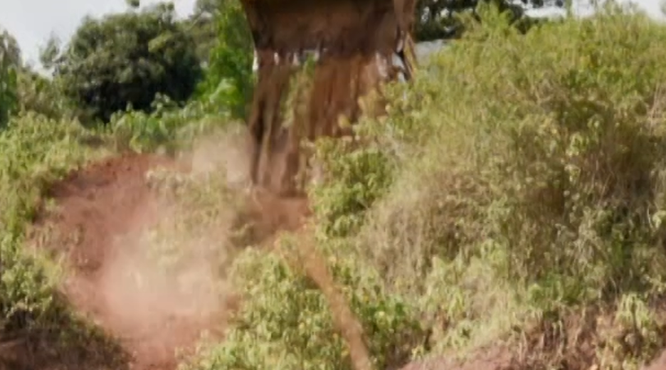 Bagger schüttet an einem Hang Erde hinunter. Uganda.