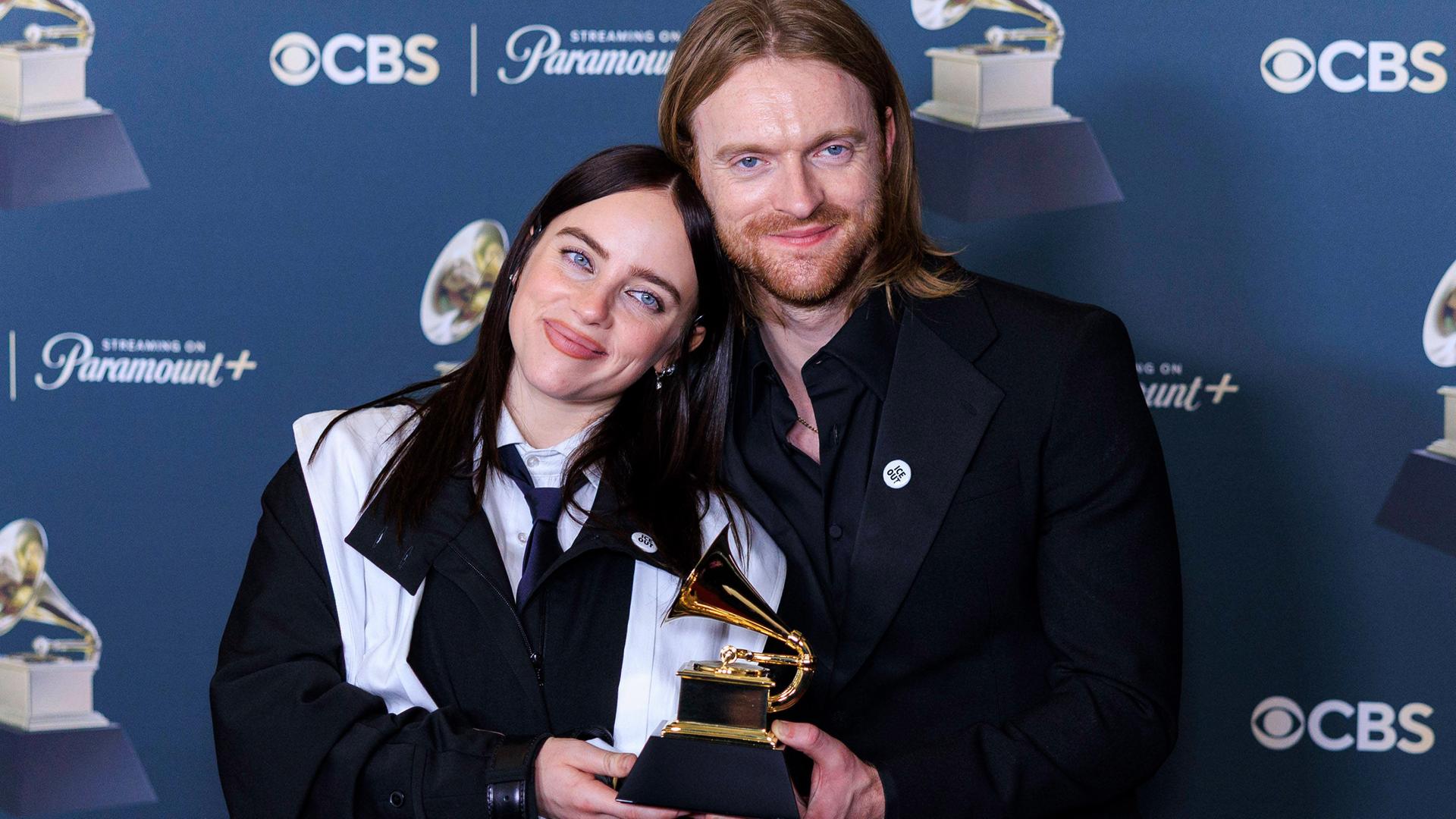 Eine junge Frau und ein junger Mann stehen nah beieinander und halten eine Trophäe in Form eines goldenen Grammophons.