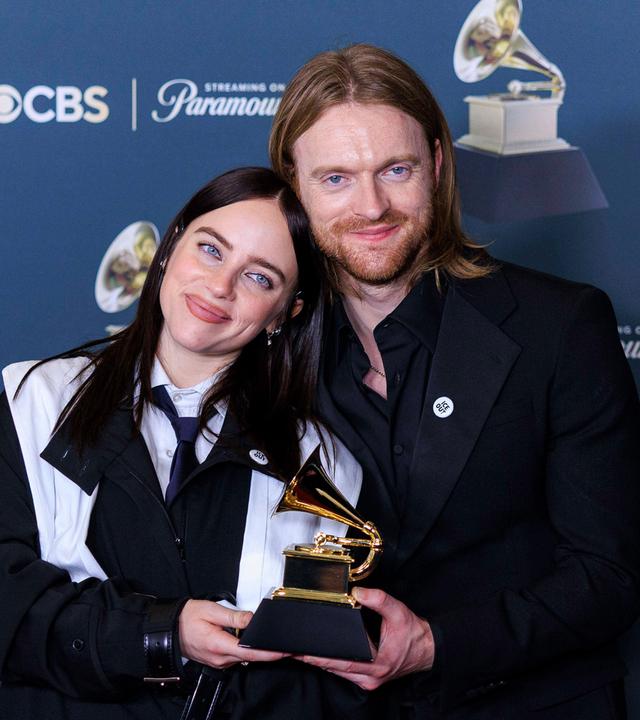 Eine junge Frau und ein junger Mann stehen nah beieinander und halten eine Trophäe in Form eines goldenen Grammophons.