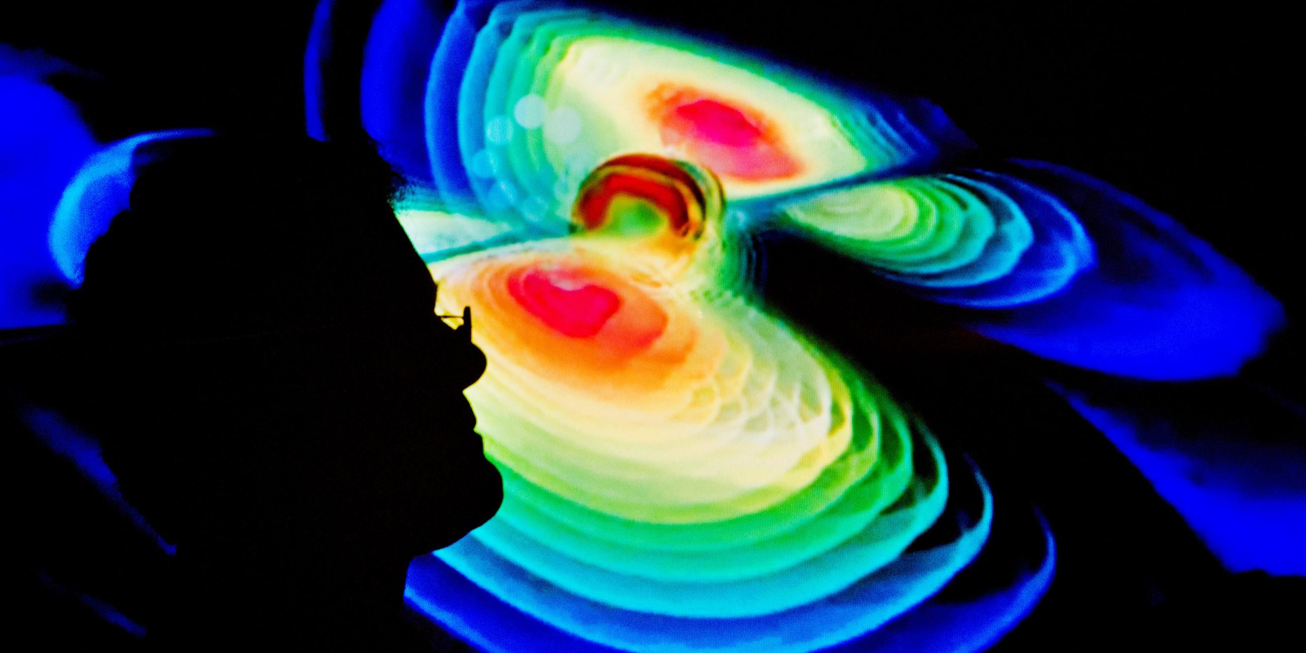 Der Schattenriss eines Wissenschaftlers vor einer Visualisierung von Gravitationswellen. 