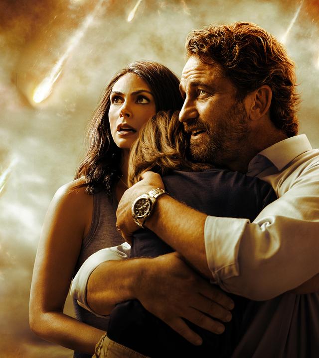 Hauptdarsteller Gerard Butler umarmt beschützend seinen kleinen Sohn. An seiner Seite steht seine Frau. Sie schauen besorgt nach oben.