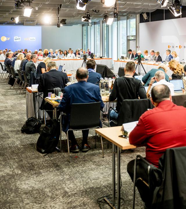 Ein großer Sitzungssaal mit vielen ZDF-Fernsehratsmitgliedern während einer laufenden Plenarsitzung, ausgestattet mit Mikrofonen, Unterlagen und Getränken. Das Bild dokumentiert die formelle Beratungssituation des Fernsehrats.