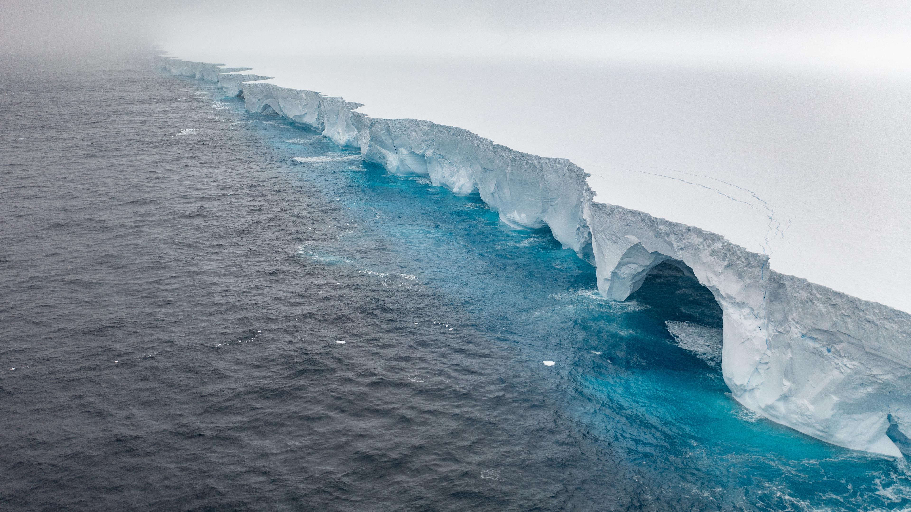 Eine riesige Eisfläche im Meer, aus der das Wasser bogenartige Stücke herrausbricht.