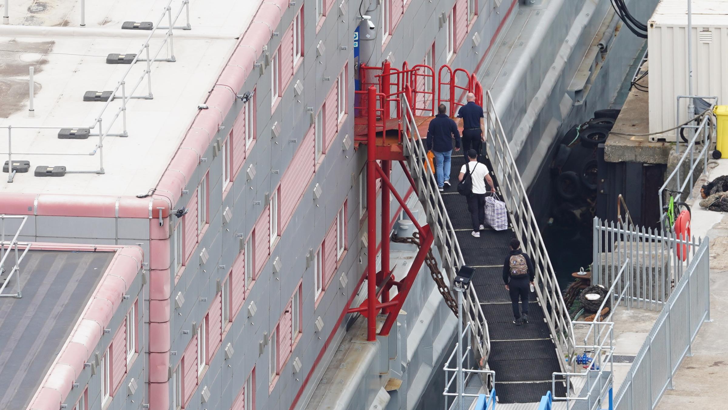 Großbritannien, Portland: Menschen gehen im Hafen von Portland an Bord des Unterkunftsschiffs "Bibby Stockholm".