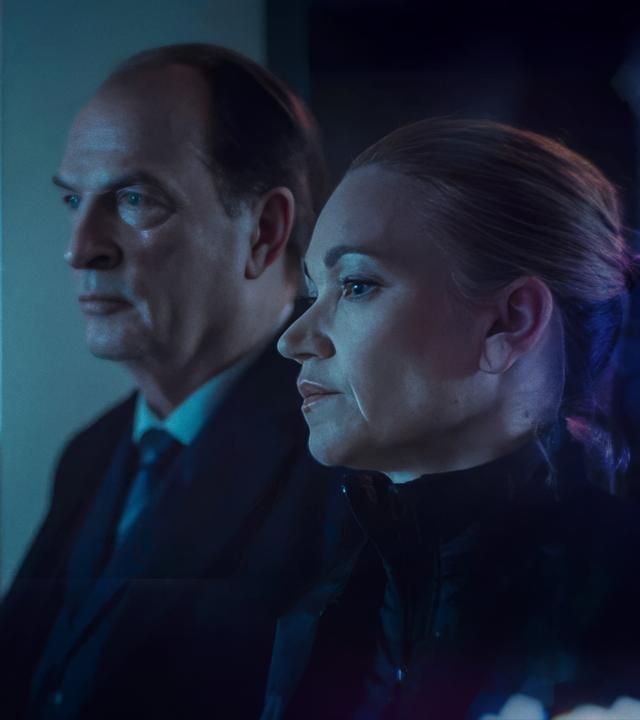 Sarah Kohr (Lisa Maria Potthoff), eine blonde Frau mit streng zurückgebundenen Haar, und Anton Mehringer (Herbert Knaup), ein etwas älterer Mann im Anzug, stehen an einem Fenster und blicken ernst nach draußen.