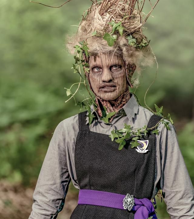 Tagsüber in einem Waldstück: Esther verwandelt sich mehr und mehr in einen Baum. Ihr Gesicht hat Ähnlichkeit mit einem Baumstamm, auf ihrem Kopf und an den Armen wachsen Blätter.