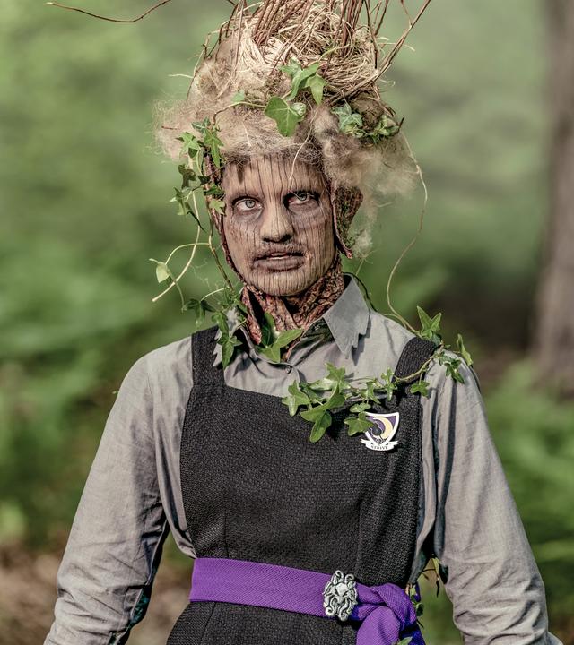 Tagsüber in einem Waldstück: Esther verwandelt sich mehr und mehr in einen Baum. Ihr Gesicht hat Ähnlichkeit mit einem Baumstamm, auf ihrem Kopf und an den Armen wachsen Blätter.