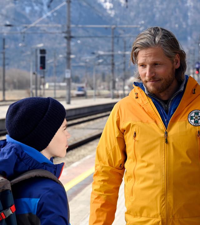 "Die Bergretter - Grüner Mond": Bergretter Markus (Sebastian Ströbel) steht am Bahnsteig zwischen Elias (Finlay Hartinger) und Bastian (Tommy Schlesser) und blickt aufmunternd den Jungen an.