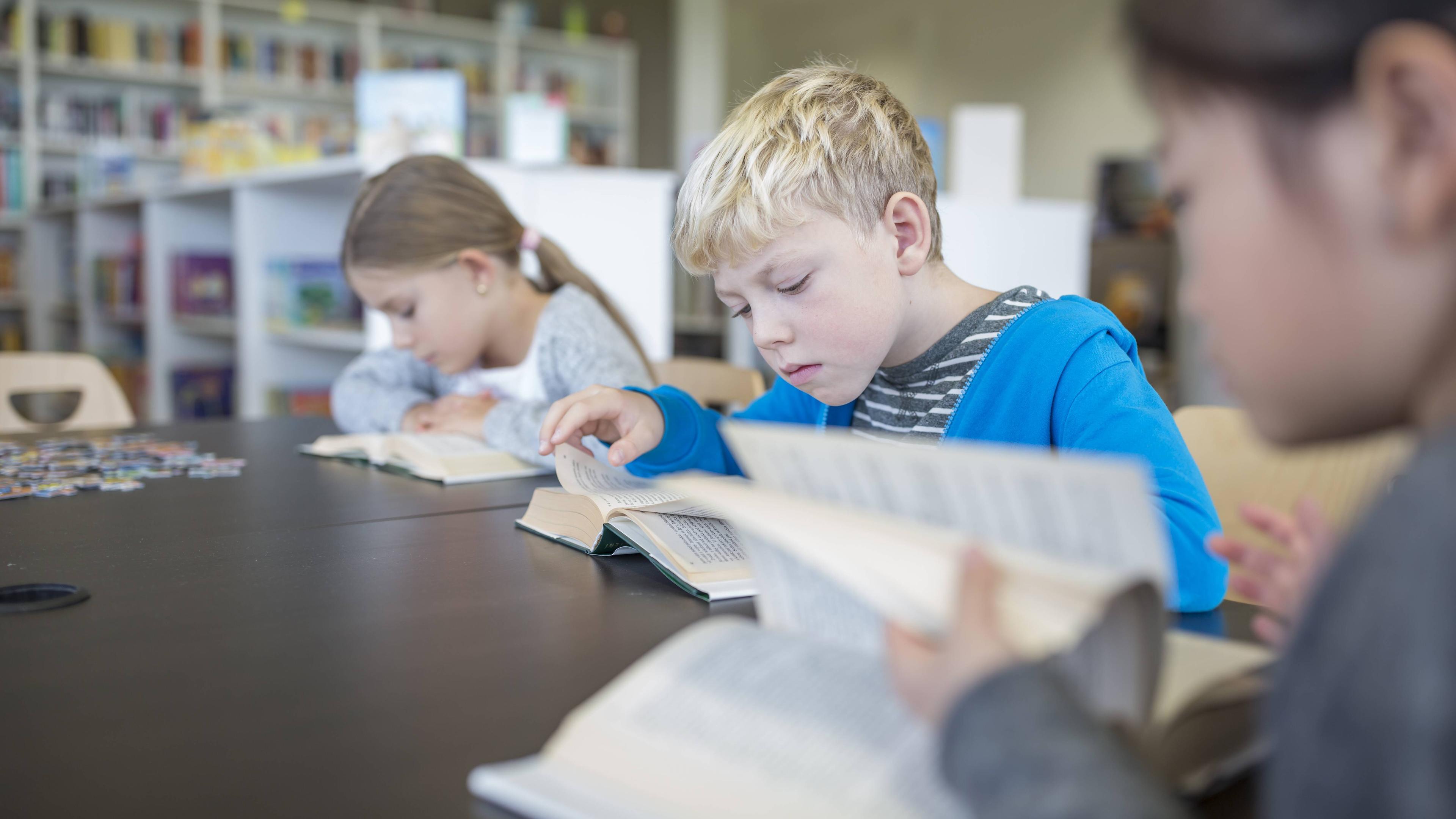 Grundschüler lesen Bücher auf dem Tisch im Pausenraum einer Schule 
