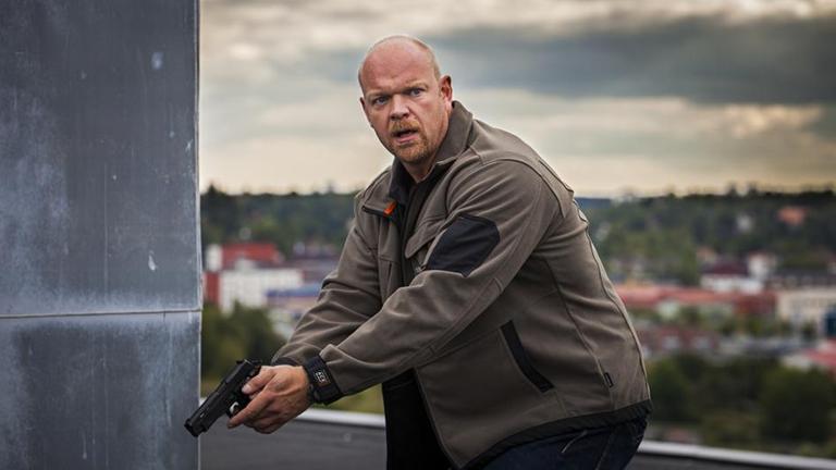 Gunnar Nyberg (Magnus Samuelsson) steht auf einem Dach mit vorgehaltener Pistole.