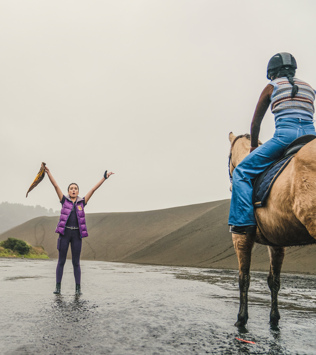 Nicole und Caroline sitzen auf ihren Pferden und warten auf das Startsignal von Bianca, die ihre Arme ausgestreckt nach oben hält. In ihrer rechten Hand hält sie ein Tuch.