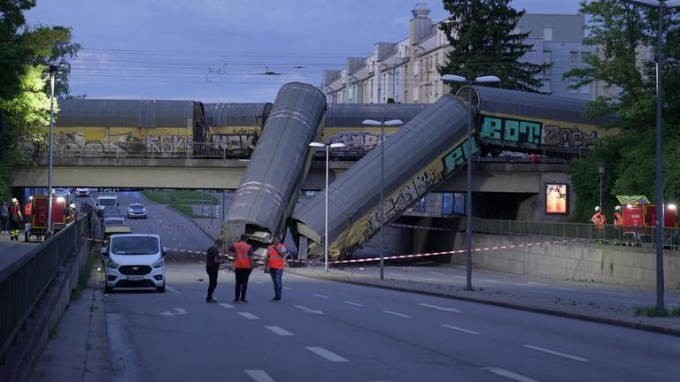 0.06.2026, Bayern, München: Zwei Waggons eines Güterzugs liegen auf einer Straße, nachdem sie von einer Brücke gestürzt sind.