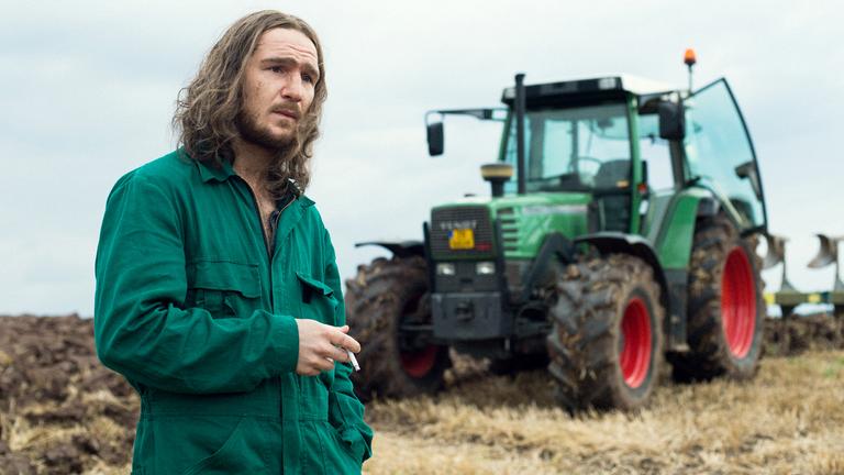 "Gutland": Jens (Frederick Lau) steht auf einem Feld vor einem Traktor.