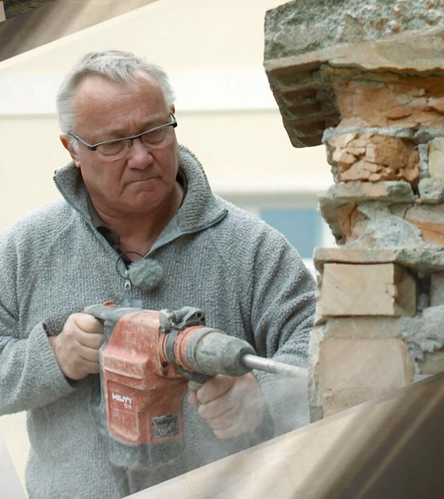 älterer Mann mit Abbruchhammer arbeitet an Ziegelmauer