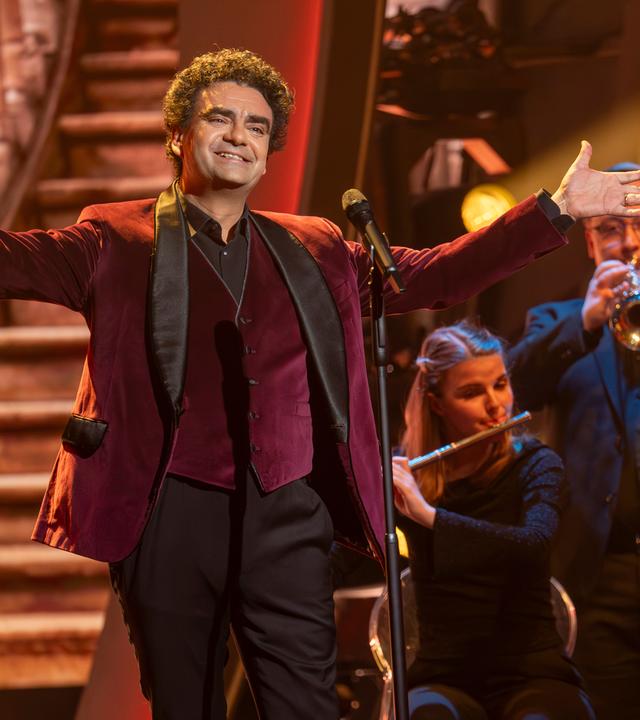 "Die Giovanni Zarrella Show – Kleine Stars ganz groß": Rolando Villazón steht mit weit ausgebreiteten Armen vor einem Mikrofon auf der Bühne. Im Hintergrund befinden sich zwei Orchestermusiker mit Trompete und Querflöte.