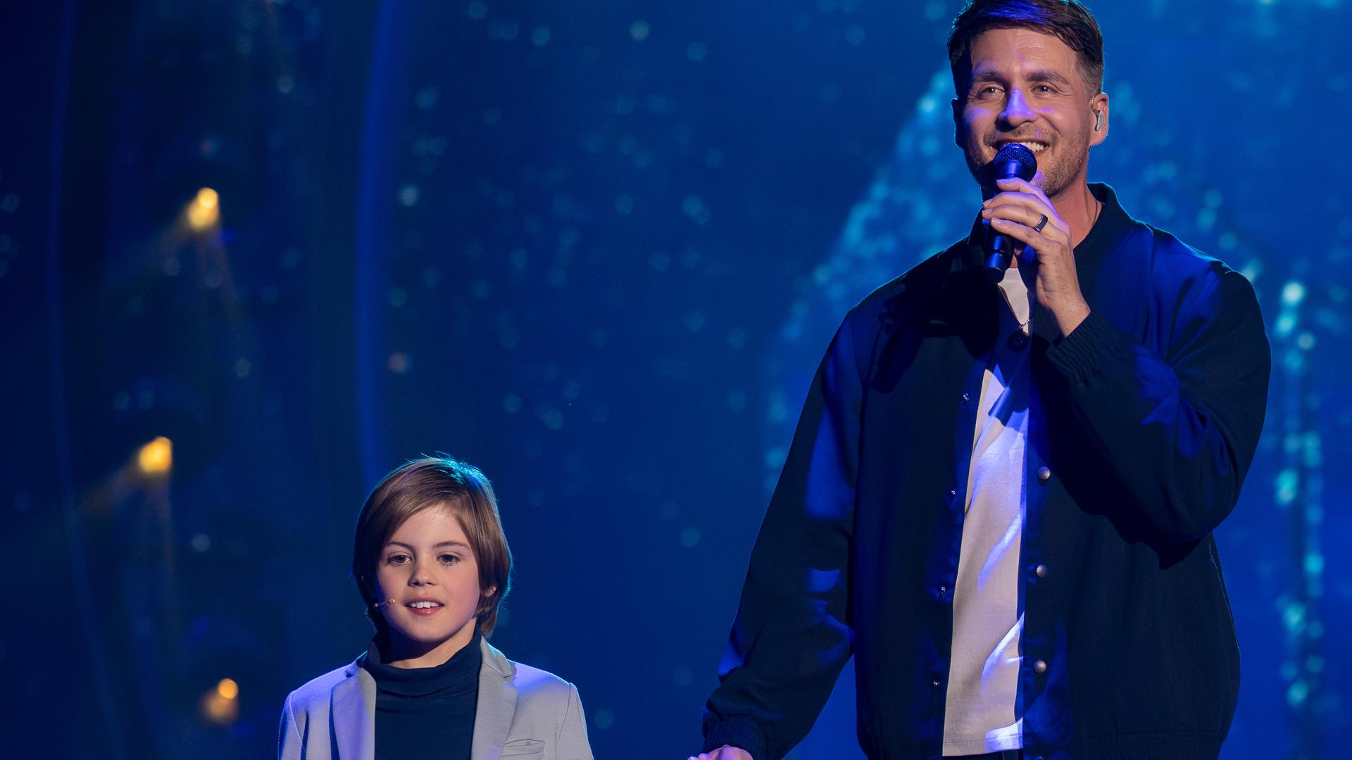 "Die Giovanni Zarrella Show – Kleine Stars ganz groß": Alexander Klaws läuft mit seinem Sohn Lenny über die Bühne, die mit Bodennebel bedeckt ist. Alexander hält Lenny an der Hand und singt in ein Mikrofon.