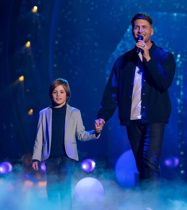 "Die Giovanni Zarrella Show – Kleine Stars ganz groß": Alexander Klaws läuft mit seinem Sohn Lenny über die Bühne, die mit Bodennebel bedeckt ist. Alexander hält Lenny an der Hand und singt in ein Mikrofon.