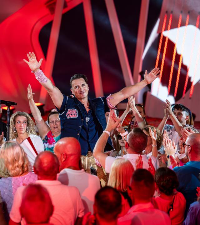 "Die Giovanni Zarrella Show - Die große Sommerparty": Andreas Gabalier steht inmitten des Publikums in der Arena des "Fernsehgartens". Beide Arme hat er nach oben gestreckt und lächelt zu den Menschen, die klatschend und feiernd zu ihm schauen.