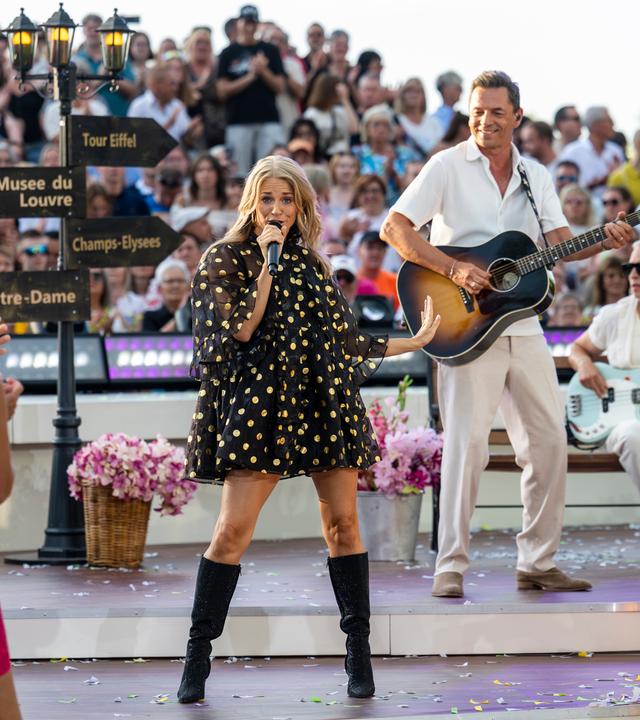 "Die Giovanni Zarrella Show - Die große Sommerparty": Julia Lindholm und der Gitarrist und Bassist der Live-Band stehen auf der Bühne. Sie singt und ist umgeben von Publikum. Die Bühne ist dekoriert mit einer Laterne und Hinweisschildern von Pariser Sehenswürdigkeiten.
