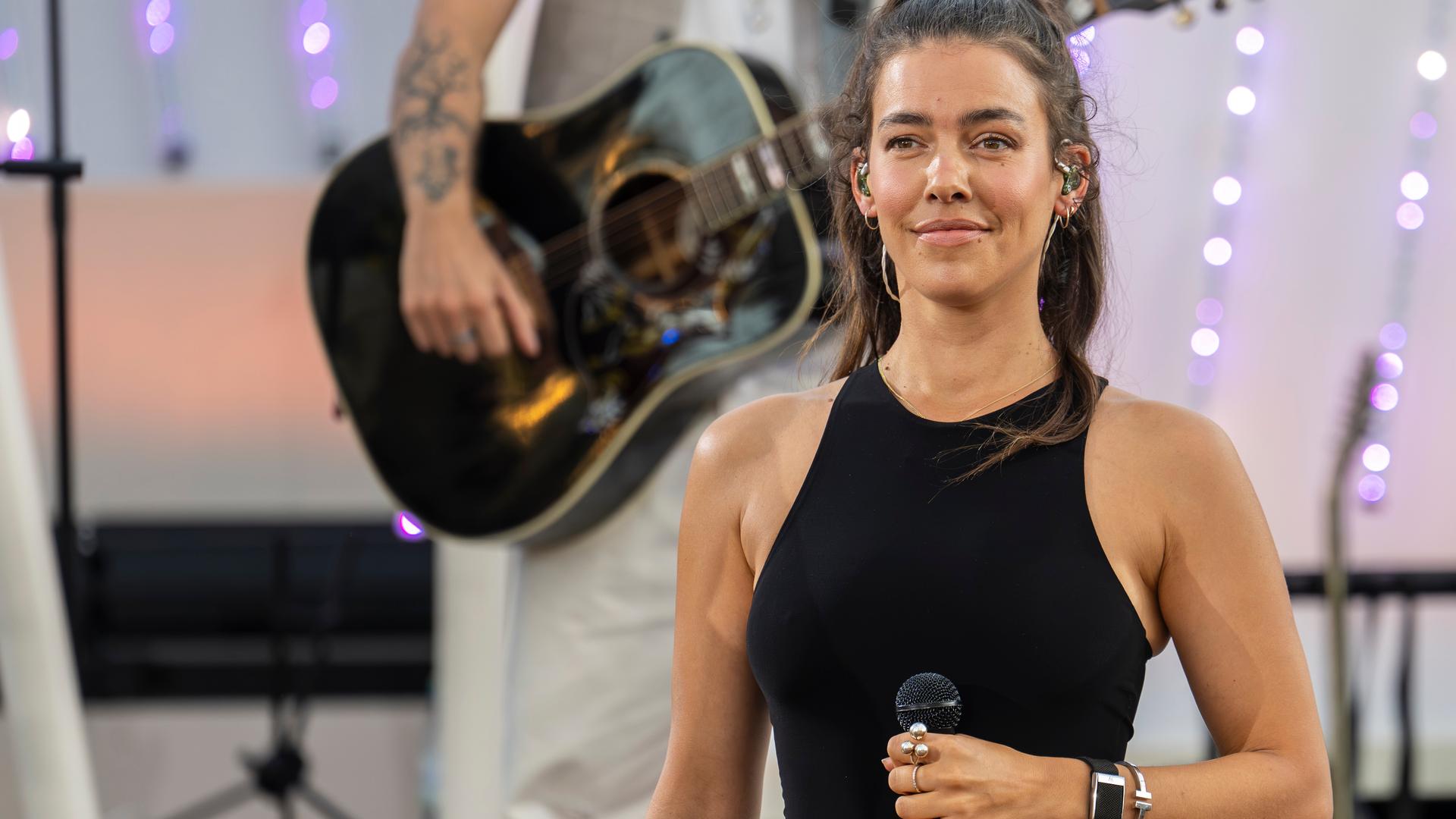 "Die Giovanni Zarrella Show - Die große Sommerparty": Sängerin Alina Süggeler steht lächelnd auf der Bühne und hält ein Mikrofon in der Hand. Im Hintergrund steht ein Musiker mit Akustikgitarre.