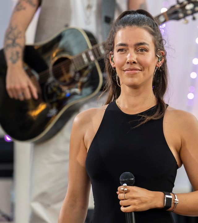 "Die Giovanni Zarrella Show - Die große Sommerparty": Sängerin Alina Süggeler steht lächelnd auf der Bühne und hält ein Mikrofon in der Hand. Im Hintergrund steht ein Musiker mit Akustikgitarre.