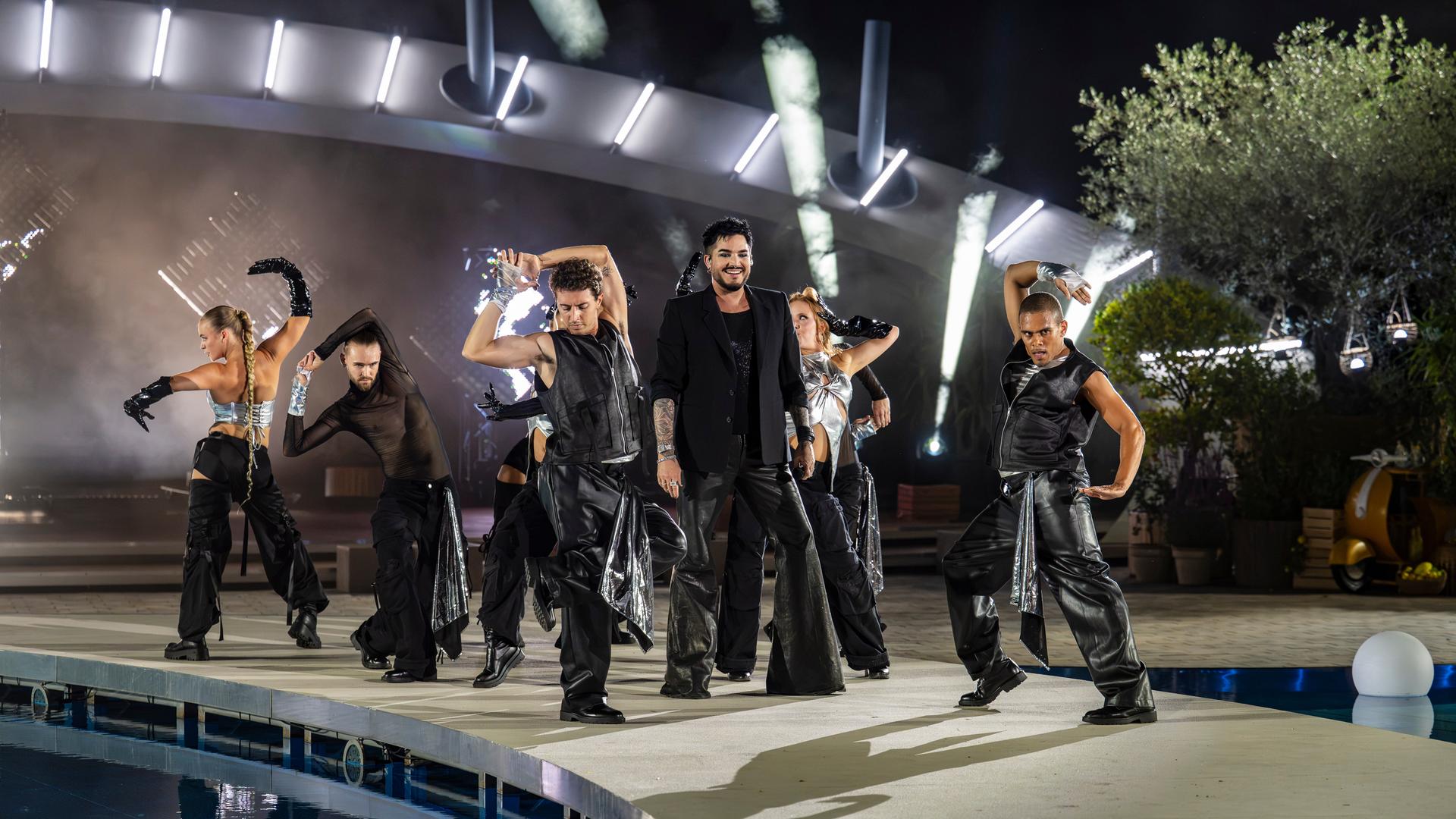 "Die Giovanni Zarrella Show - Die große Sommerparty": Adam Lambert steht auf der Bühne am Pool des "Fernsehgartens". Um ihn herum tanzen Tänzerinnen und Tänzer. Der Himmel ist dunkel, es leuchten einzelne helle Lichtkegel von Scheinwerfern. Der Sänger und die Tänzer tragen schwarze-silberne Bühnenoutfits.