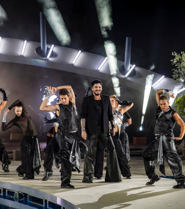 "Die Giovanni Zarrella Show - Die große Sommerparty": Adam Lambert steht auf der Bühne am Pool des "Fernsehgartens". Um ihn herum tanzen Tänzerinnen und Tänzer. Der Himmel ist dunkel, es leuchten einzelne helle Lichtkegel von Scheinwerfern. Der Sänger und die Tänzer tragen schwarze-silberne Bühnenoutfits.