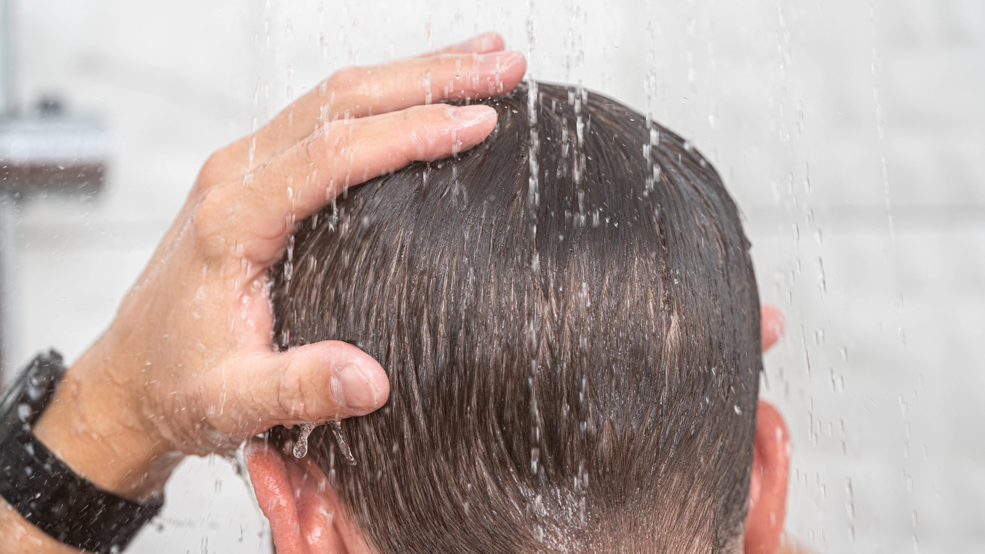 Kopf eines Mannes unter der Dusche, die Haare sind nass.