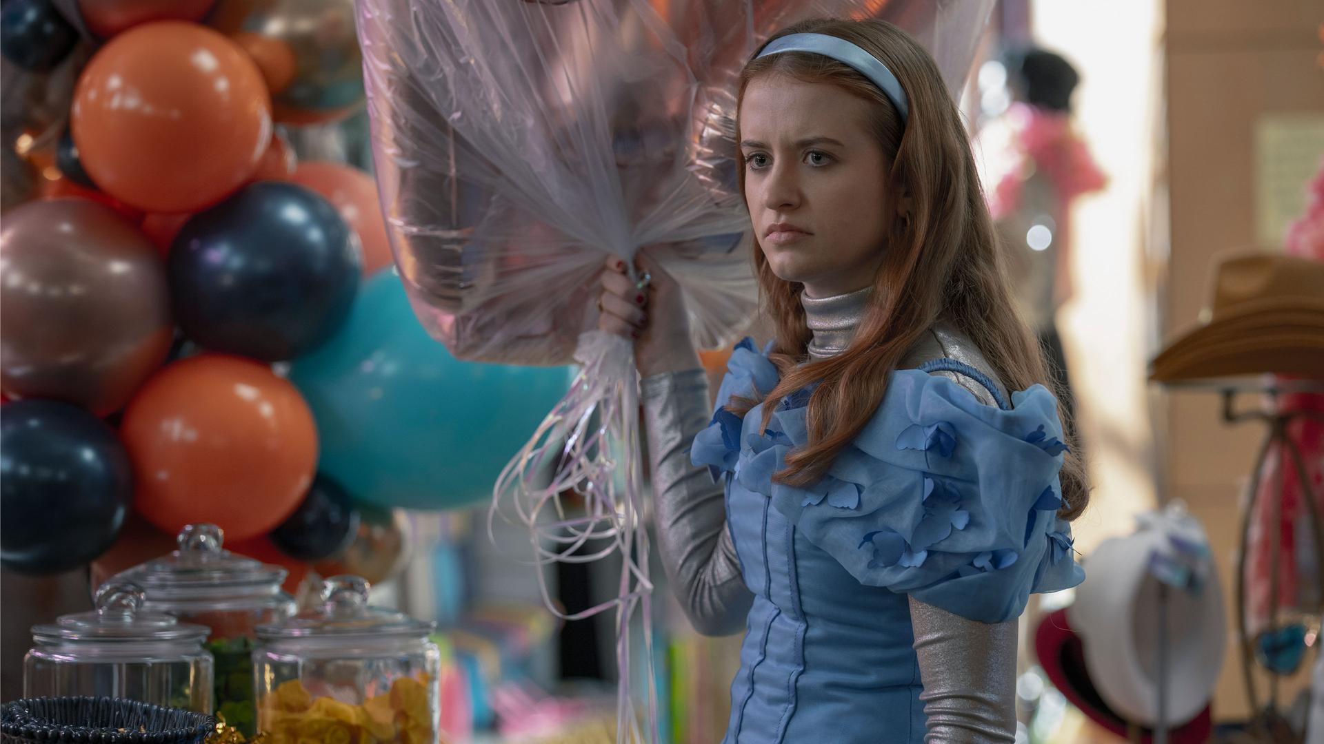 "Extraordinary - Habenichtse": Jen (Máiréad Tyers) steht grimmig blickend in einem Geschäft. In ihrer Hand hält sie ein Strauß Helium-Luftballons.