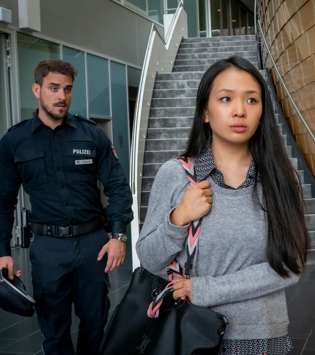 "Notruf Hafenkante - Härtefall": Im Vordergrund steht Gina Weskamp (Andrea Guo). Sie trägt eine Umhängetasche über ihrer rechten Schulter, die sie festhält. Sie blickt nachdenklich ins Leere. Hinter ihr stehen der Polizist Kris Freiberg (Marc Barthel) und seine Kollegin Pinar Aslan (Abi Era). Beide blicken Gina hinterher.