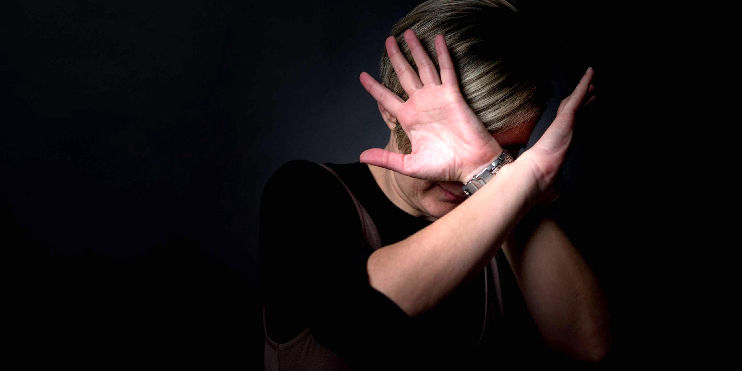 Eine Frau hebt schützend die Hände vor ihr Gesicht, um sich vor Schlägen zu schützen