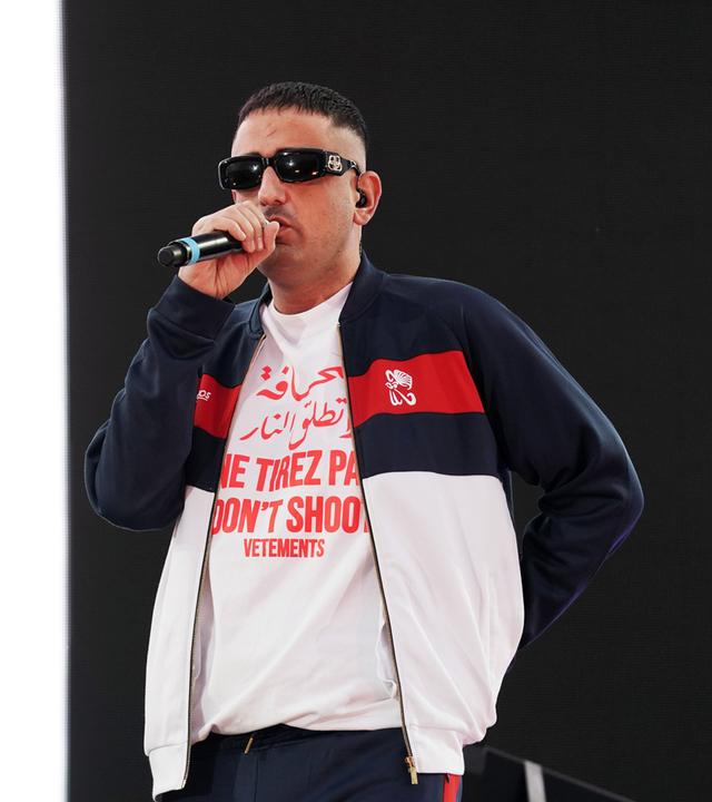 Ein Mann mit Kurzhaarschnitt und Sonnenbrille singt auf einer Bühne in ein Mikro.