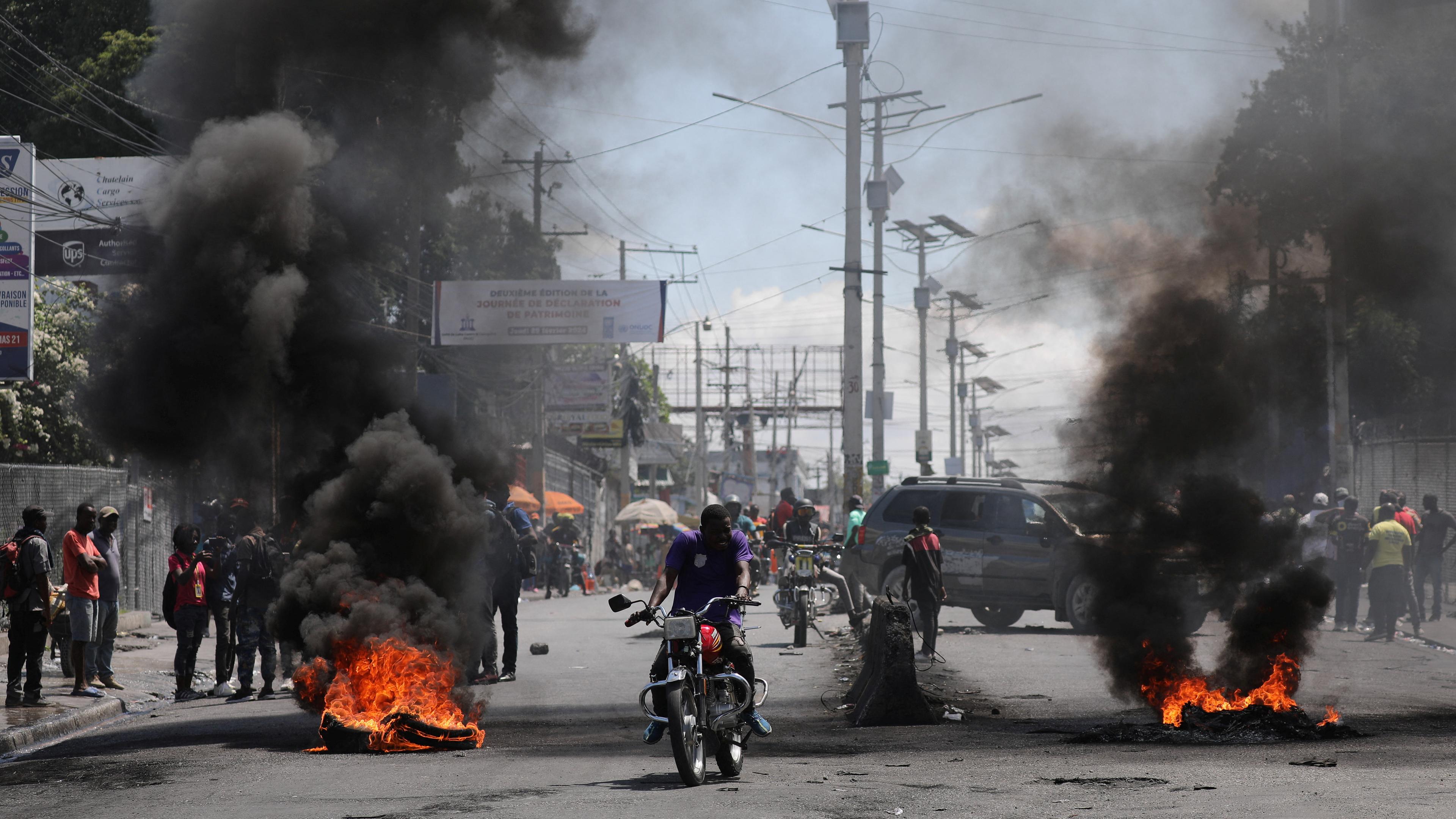 Motorradfahrer fahren während eines Protests an einer brennenden Barrikade vorbei.