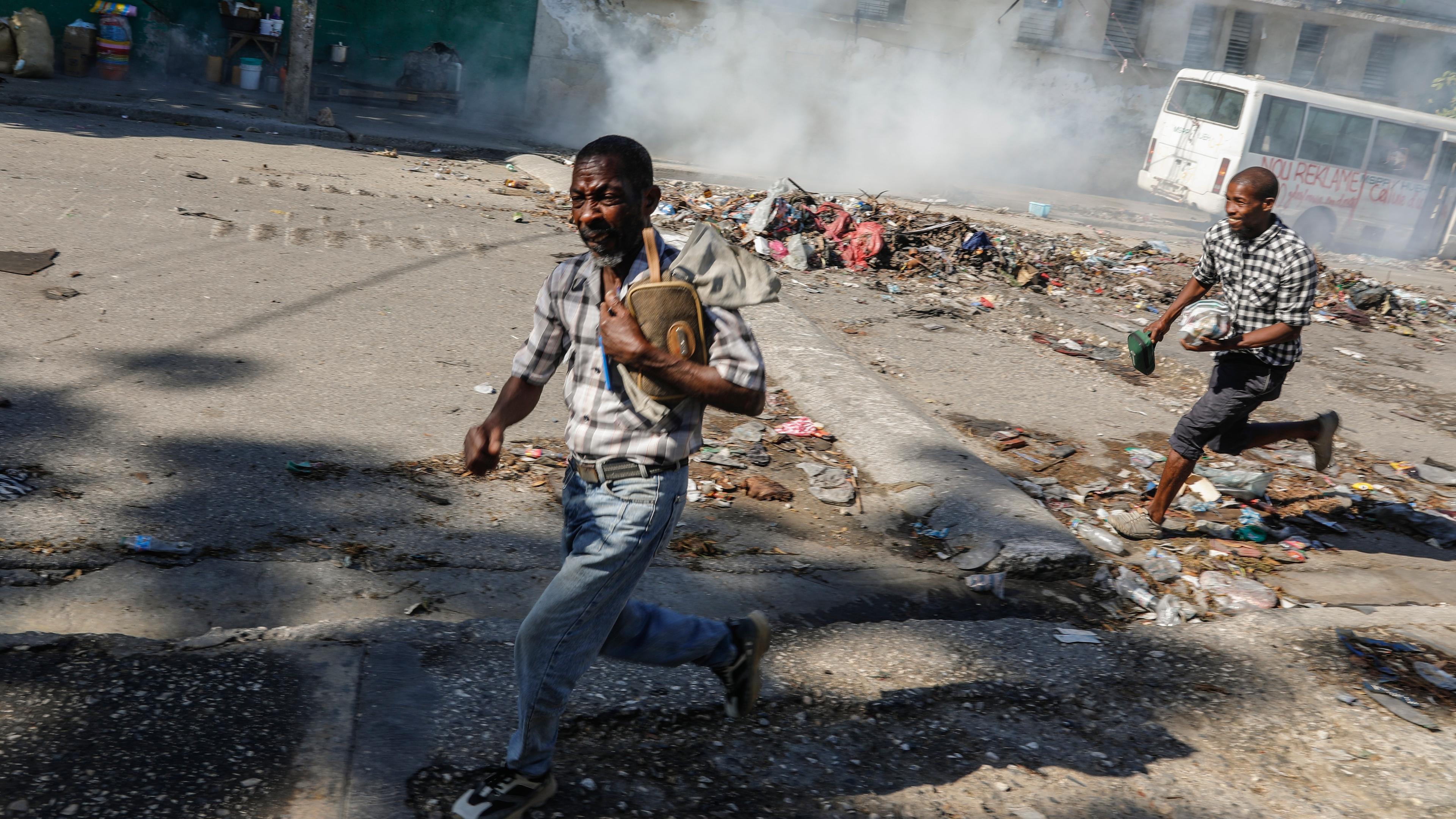 Männer gehen in Deckung, als die Bereitschaftspolizei Tränengas einsetzt, um die Menschen in der Nähe des Nationalpalastes in Port-au-Prince, Haiti, zu vertreiben.