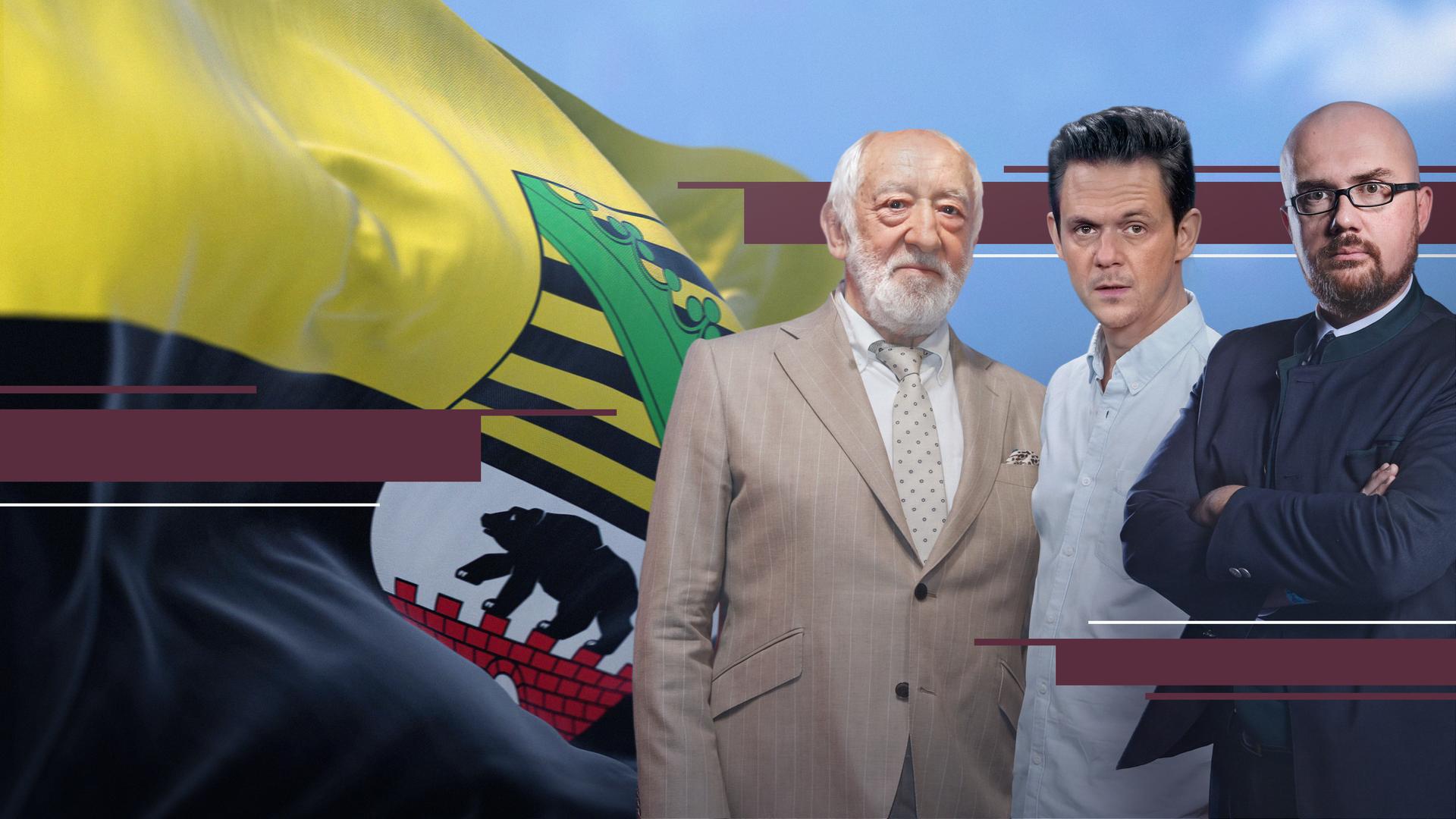 Dieter Hallervorden, Jo Schück und Hans-Tomas Tillschneider stehen nebeneinander und schauen den Betrachter an. Im Hintergrund flattert eine Sachsen-Anhalt-Flagge.