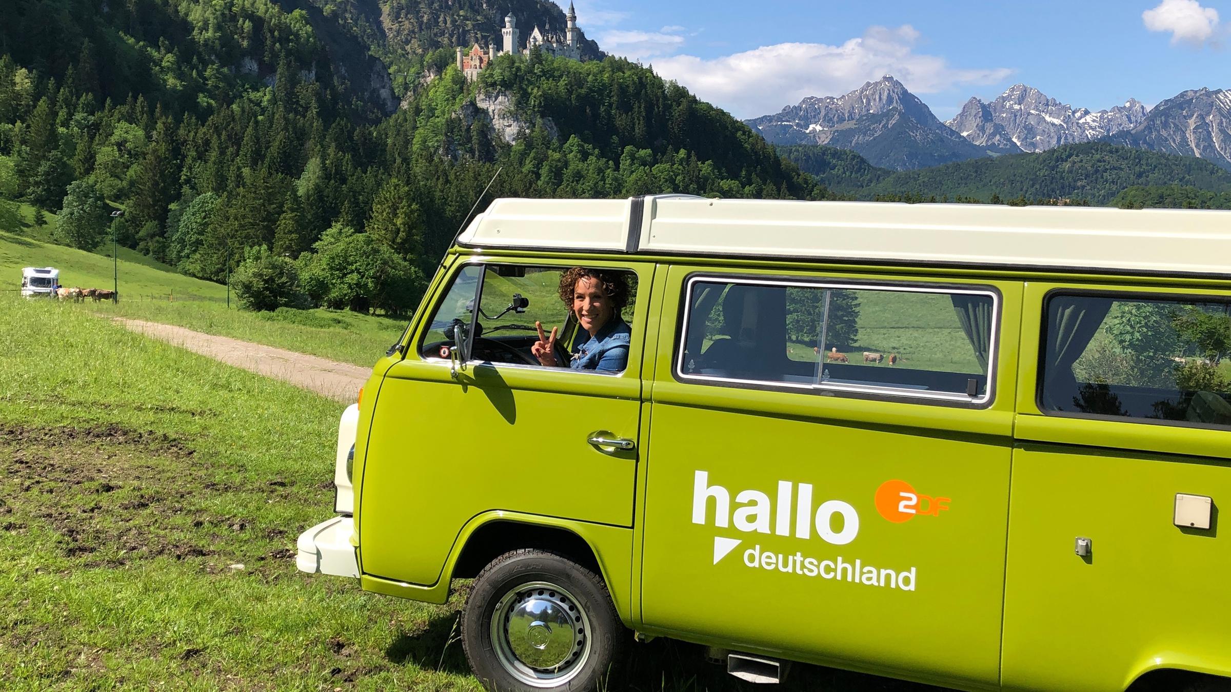 Lissy Ishag sitzt im Bulli, im Hintergrund Schloss Neuschwanstein im Allgäu.