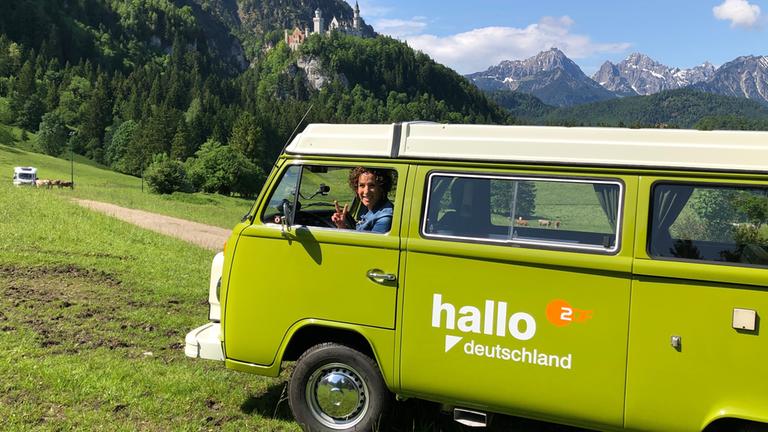 Lissy Ishag sitzt im Bulli, im Hintergrund Schloss Neuschwanstein im Allgäu.