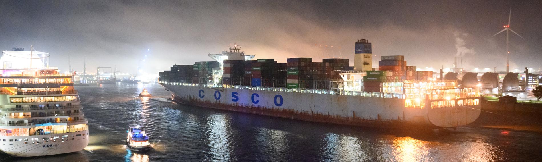 Der Hamburger Hafen bei Nacht. Ein Schiff mit dem Aufdruck "Cosco" läuft in den Hafen ein.