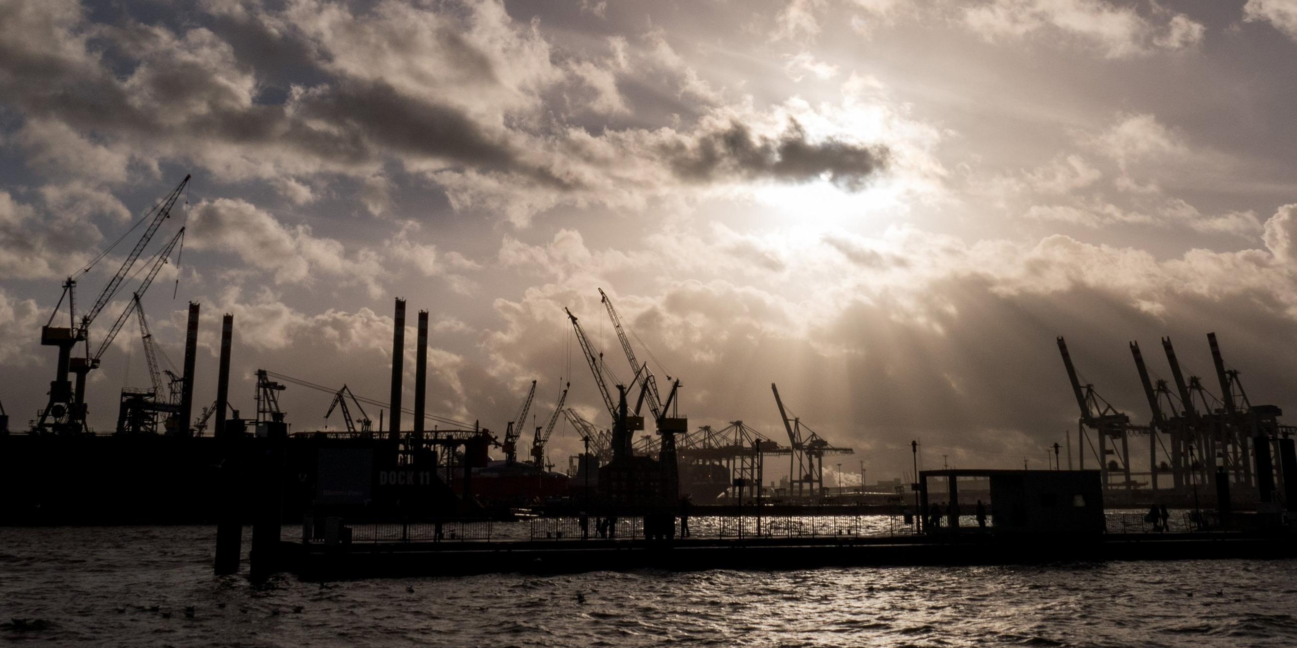 Hamburg: Durch dunkle Regenwolken scheint etwas Sonne über den Hafenanlagen in Hamburg. Archivbild