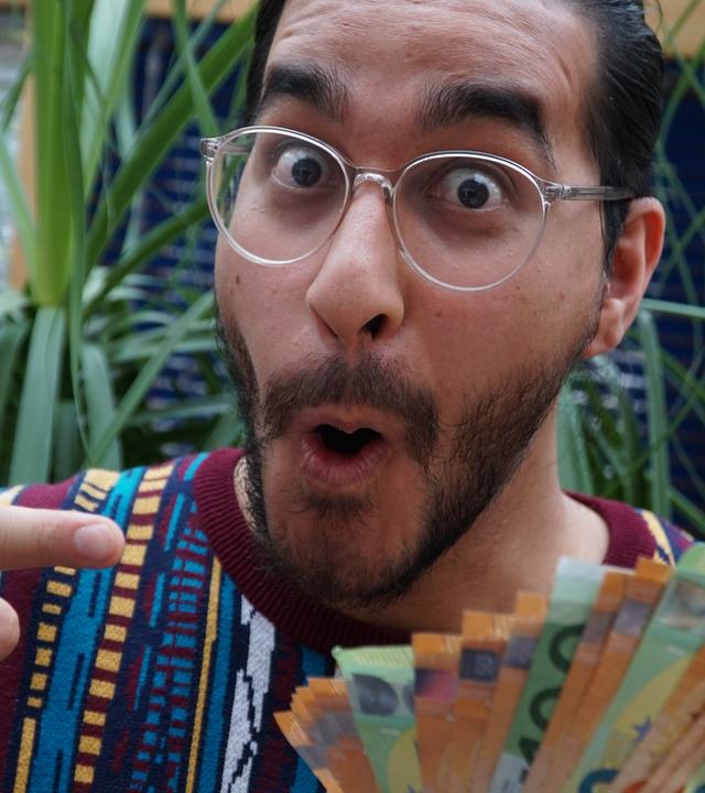 Ein junger Mann hält fröhlich-staunend ein Bündel Gelscheine in der Hand.