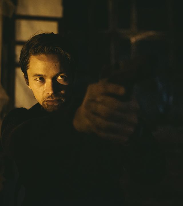 "Hamilton - Undercover in Stockholm": Agent Hamilton (Jakob Oftebro) steht im Halbdunkel mit einer Pistole im Anschlag und zielt rechts aus dem Bild.