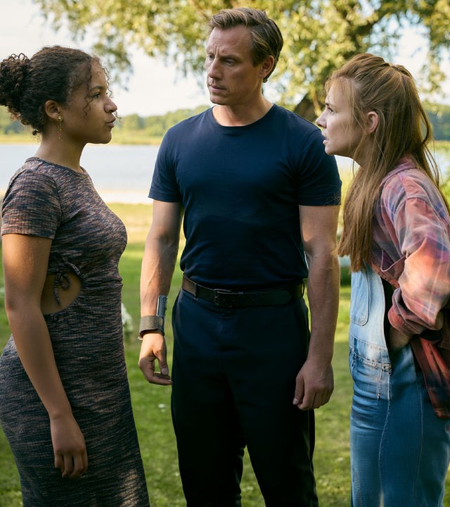 "Dr. Nice - Hand aufs Herz": In einer grün mit Sträuchern bewachsenen Landschaft steht Charlie (Josefine Preuß) wütend Lea (Maj Borchardt) gegenüber. Leas "Vater" Moritz Neiss (Patrick Kalupa) steht zwischen den beiden und schaut Lea fragend an. In der Ferne ist ein kleiner See zu sehen.