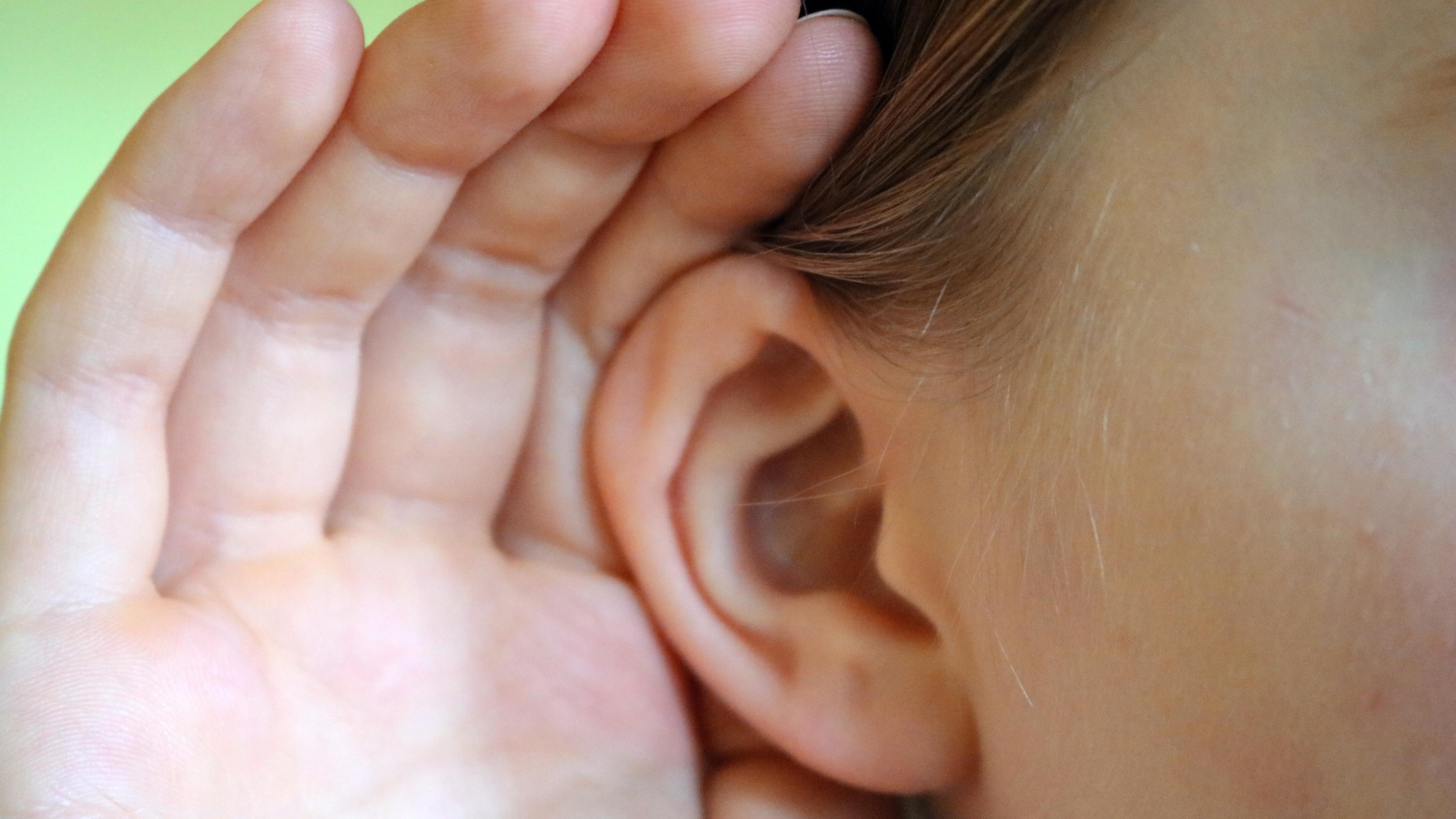 Ein Kind hält sich eine Hand ans Ohr.