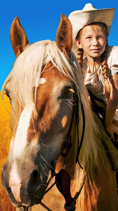 In einem goldgelben Getreidefeld vor strahlend blauem Himmel steht das Pferd Mississippi mit Emma (Zoë Charlotte Mannhardt) auf dem Rücken.