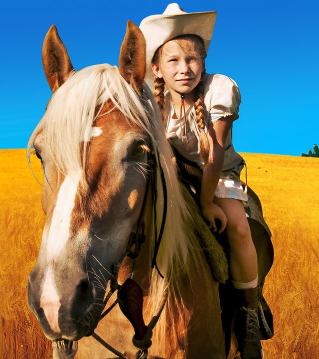 In einem goldgelben Getreidefeld vor strahlend blauem Himmel steht das Pferd Mississippi mit Emma, gespielt von Zoë Charlotte Mannhardt, auf dem Rücken.