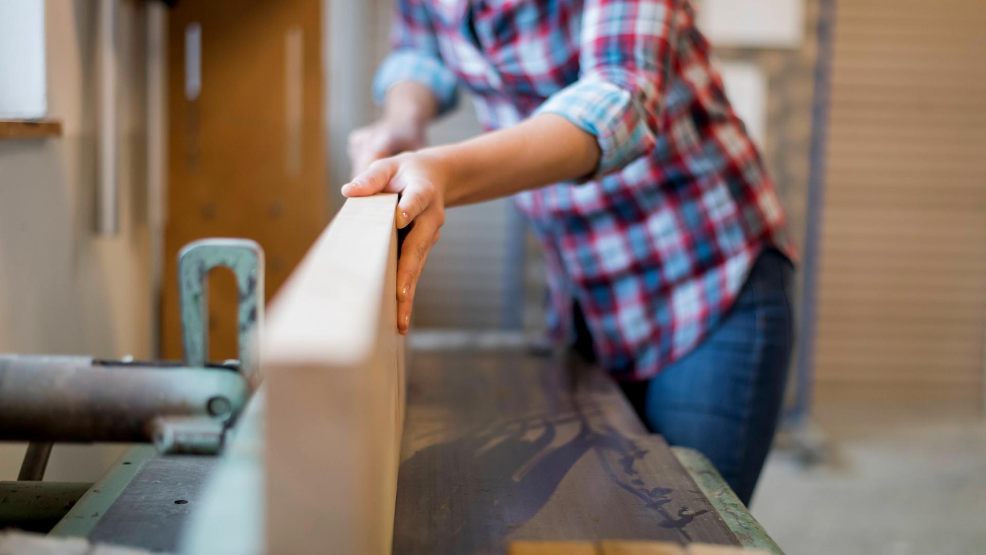Frau bedient Hobel an einer Werkbank in der Schreinerei.