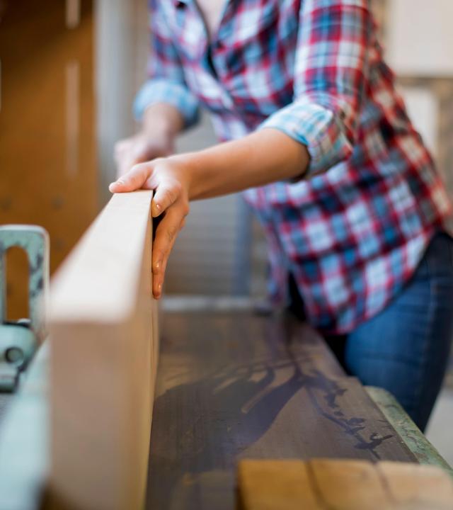 Frau bedient Hobel an einer Werkbank in der Schreinerei.