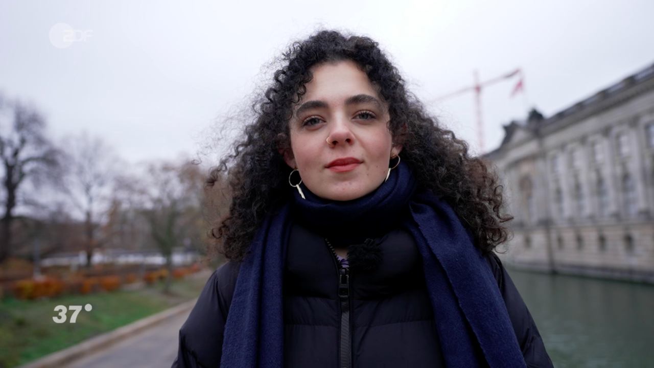 Junge Frau mit langen schwarze Locken schaut freundlich in die Kamera.