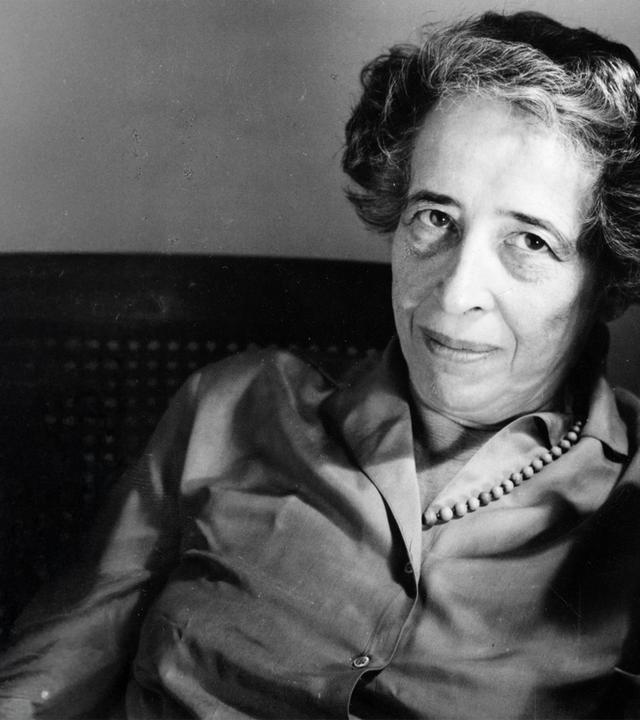 Altes Schwarz-Weiß-bild von einer Frau mittleren Alters, die sich in einem Stuhl zurücklehnt und eine rauchende Zigarette zwischen zwei Fingern hält.